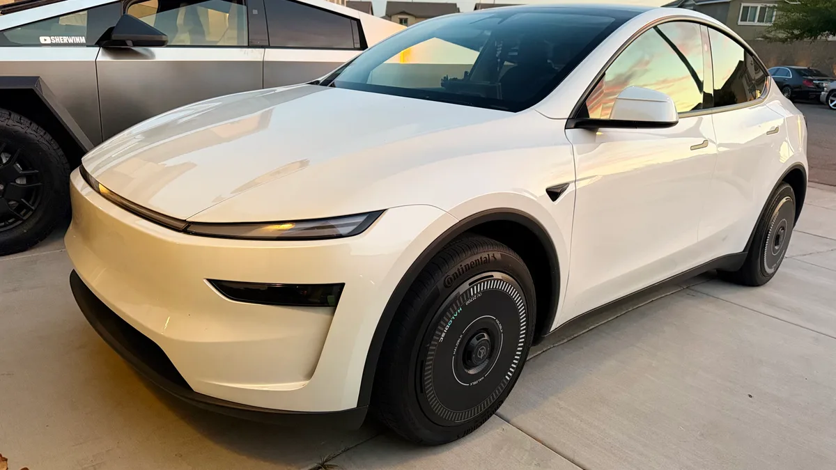 White Tesla Model Y with HALOBLK wheel covers, front-left view, parked next to a Tesla Cybertruck.