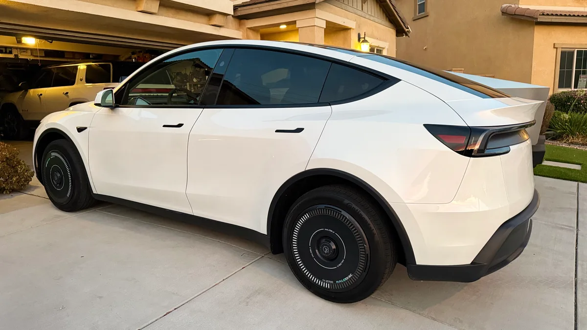 White Tesla Model Y with black HALOBLK aerodynamic wheel covers parked in a suburban driveway at dusk.