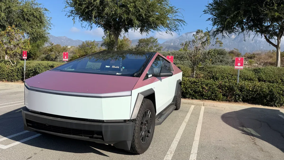 Two-tone white and plum wrapped Tesla Cybertruck parked at Tesla Service Upland with the San Gabriel Mountains behind it.