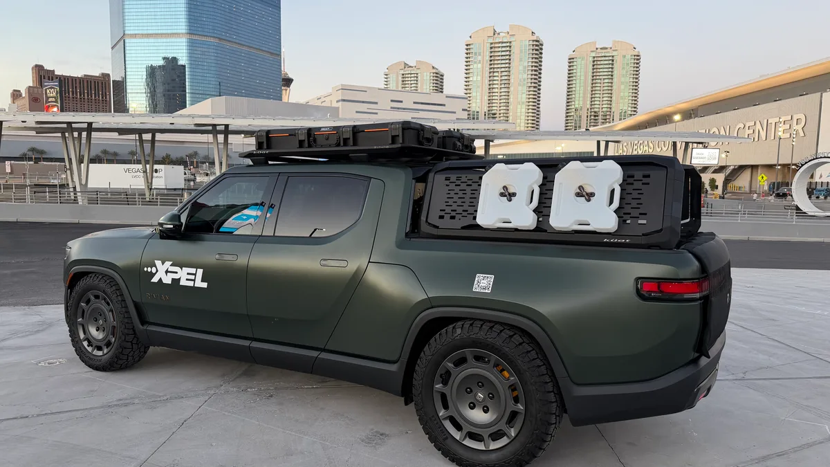 Dark green XPEL-wrapped Rivian R1T with roof rack and jerry cans parked near the Vegas Convention Center